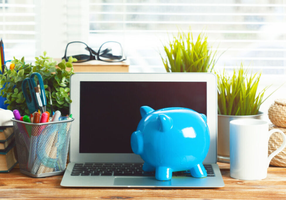 Piggy money box with laptop on wooden table