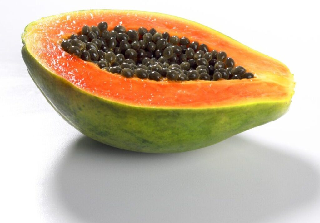 A closeup of a fresh papaya fruit sliced in half isolated on a white background