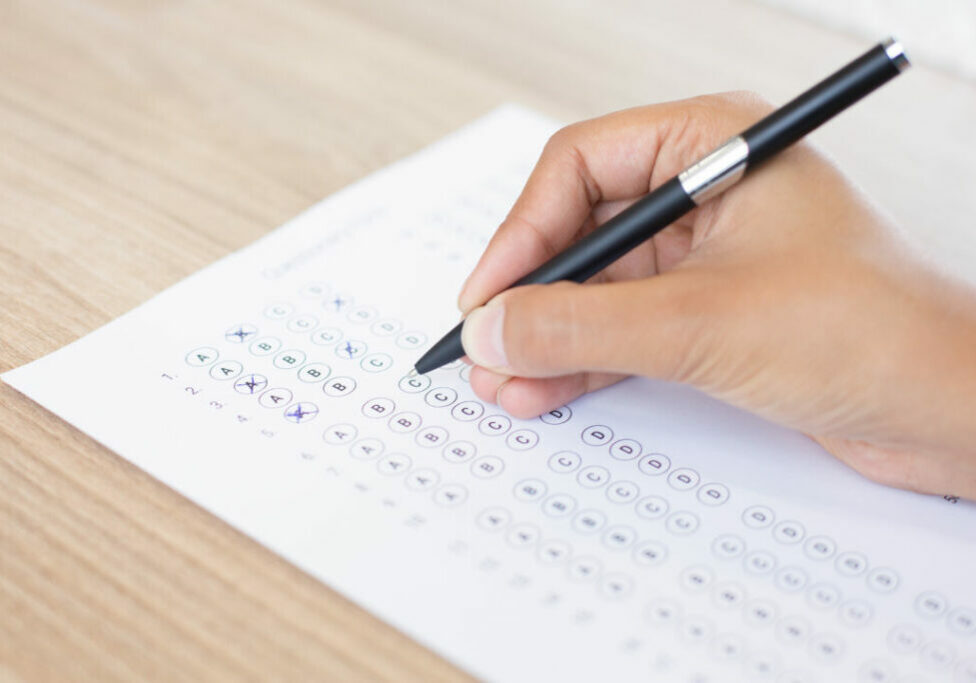 Closeup of hand holding pen and filling out questionary form on table