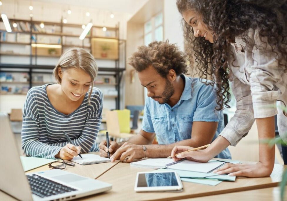 close-up-of-young-group-of-startapers-sitting-in-library-making-research-about-future-tem-project-looking-through-graphics-on-laptop-writing-new-ideas-business-teamwork-concept-1